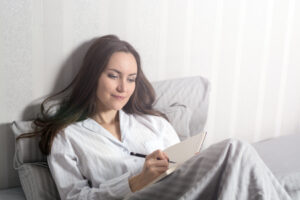 Eine Frau sitzt auf dem Bett und notiert etwas in einem kleinen Buch.