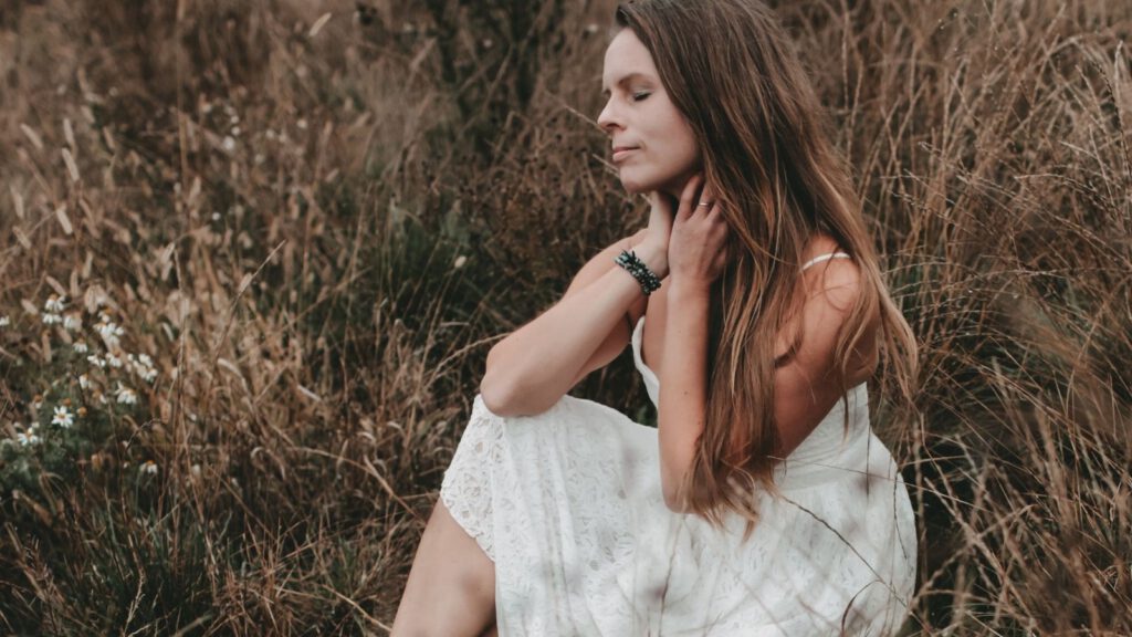 Frau sitzt in der Natur mit geschlossenen Augen und Händen auf der Brust – Verbindung zum eigenen Körper und innerer Ruhe