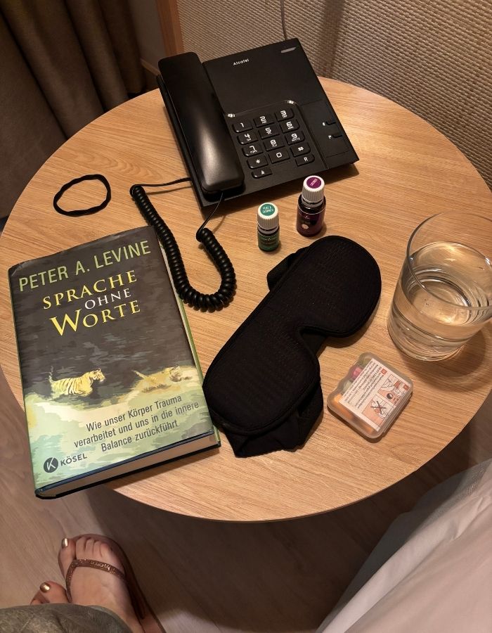 Nachttisch mit Buch, Augenmaske, Wasser und ätherischen Ölen für die Abendroutine