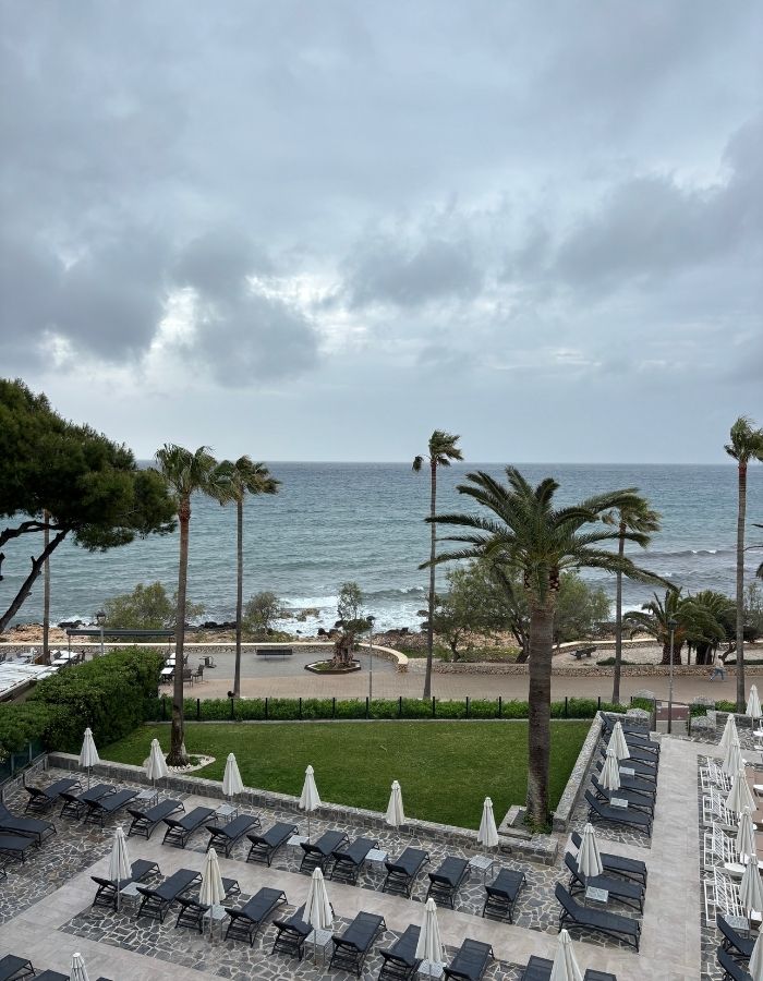 Blick vom Hotelbalkon auf Meer und Promenade in Cala Major bei bewölktem Himmel und Wellen